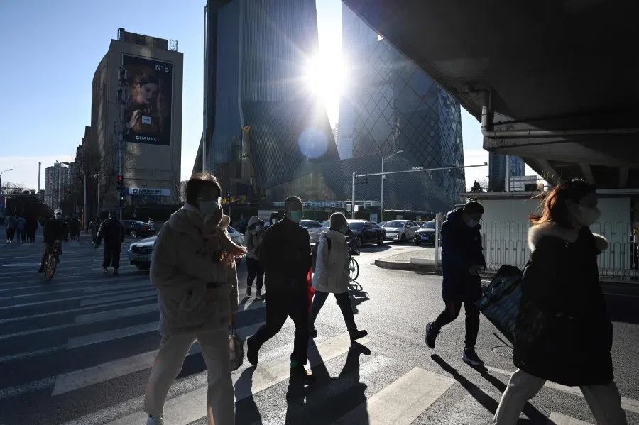 People cross a road in the central business district in Beijing on 16 December 2021. (Greg Baker/AFP)