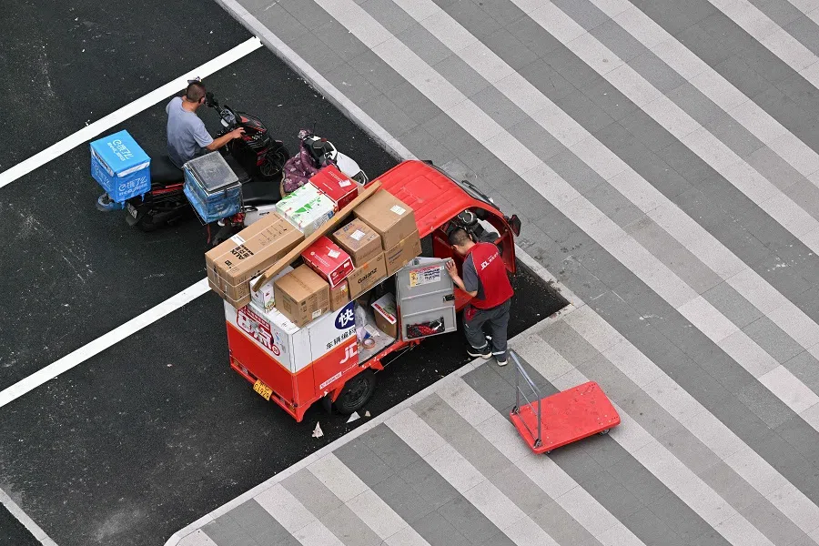 Delivery workers are seen by their vehicles at a parking lot in Beijing on 24 July 2024.