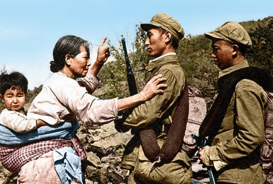 A North Korean farmer with a child on her back, tearfully describing to volunteer troops how her home was destroyed, 1951.