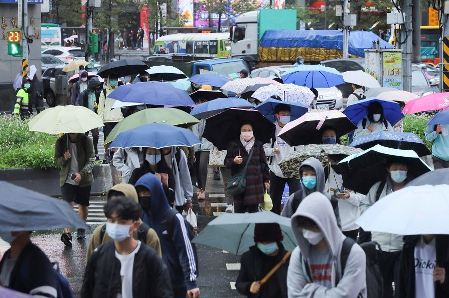 People wearing face masks and carrying umbrellas walk on the street during a rainy day in Taipei, Taiwan, 26 November 2021. (Annabelle Chih/Reuters)