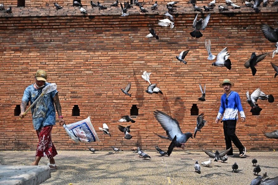 A tourist (right) stands near Ta Pae Gate for pictures as pigeons fly by in Chiang Mai on 10 April 2023. (Lillian Suwanrumpha/AFP)