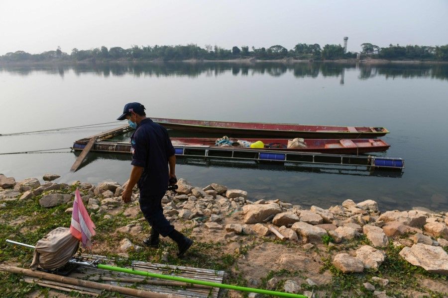 This picture taken on 15 March 2021 shows a member of a village security unit walking along the banks of the Mekong river past boats in the northern Thai region of Nong Khai, bordering Laos. (Panumas Sanguanwong/AFP)