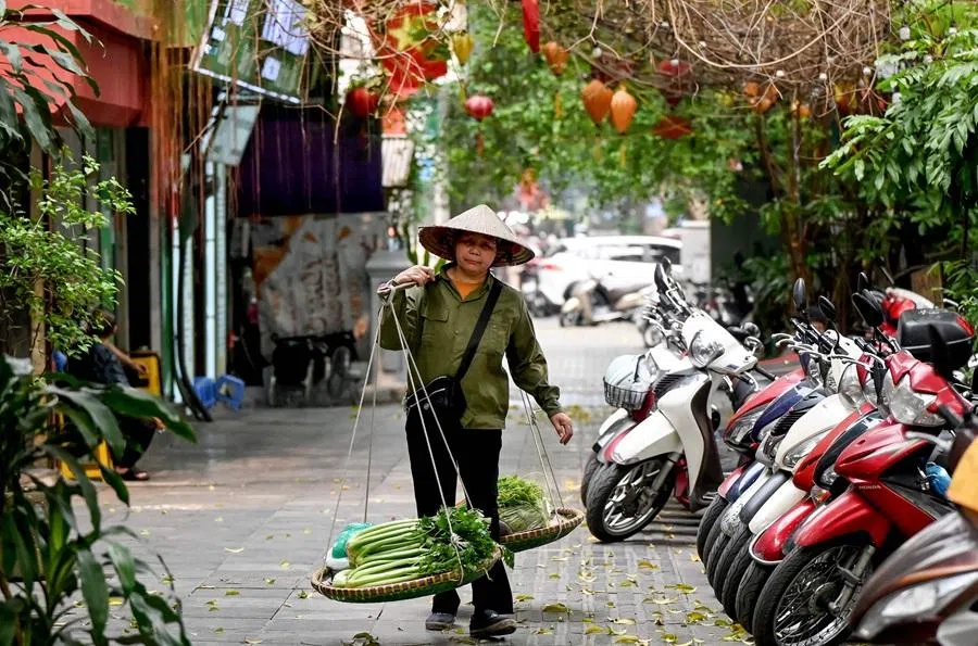 A street vendor walks down a street in Hanoi carrying vegetables for sale on 8 April 2026. (Nhac Nguyen/AFP)