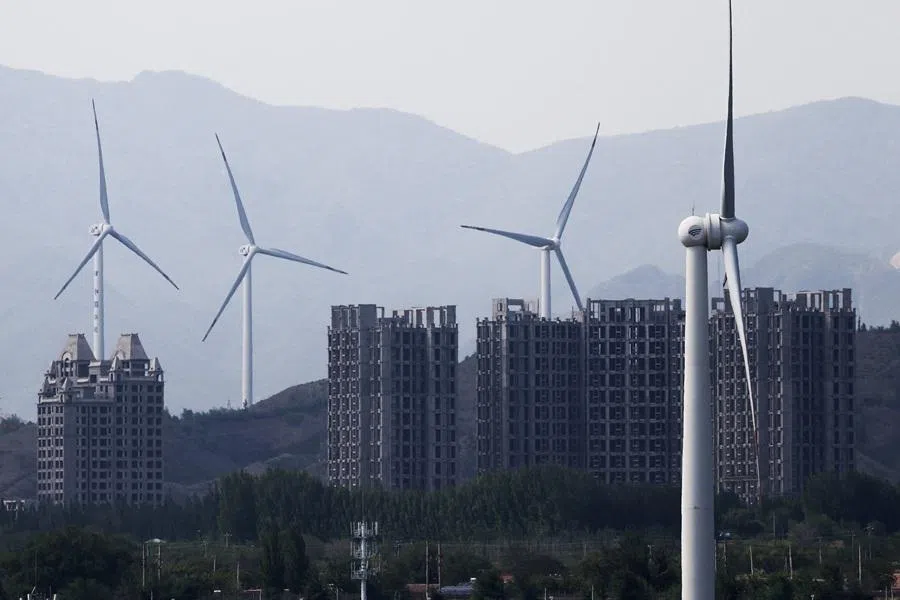 Wind turbines stand near unfinished construction of apartment blocks in Zhangjiakou, Hebei province, China, 8 May 2026. (Maxim Shemetov/Reuters)