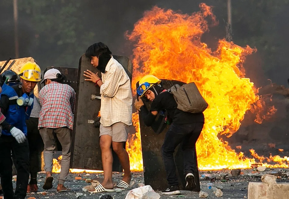 Protesters take cover behind homemade shields as they confront the police during a crackdown on demonstrations against the military coup in Yangon, Myanmar, on 16 March 2021. (STR/AFP)