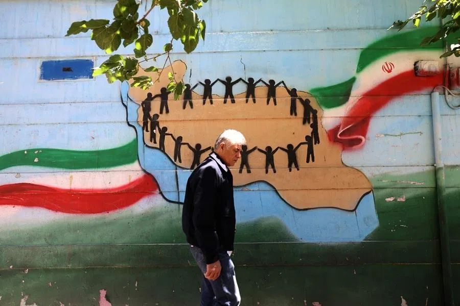 An Iranian man walks past the map of Iran, with its citizens holding hands, painted on a wall in the capital Tehran on 9 May 2026.