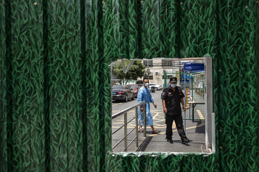 ​A security guard and a volunteer behind a fence surrounding a residential neighbourhood placed under lockdown due to Covid-19 in Shanghai, China, on 6 July 2022. (Qilai Shen/Bloomberg)