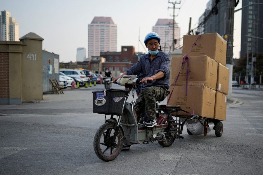 A delivery worker wearing a protective mask rides an electric scooter across a street ahead of Alibaba's Singles' Day shopping festival, following a coronavirus disease (Covid-19) outbreak in Shanghai, China, 10 November 2022. (Aly Song/Reuters)