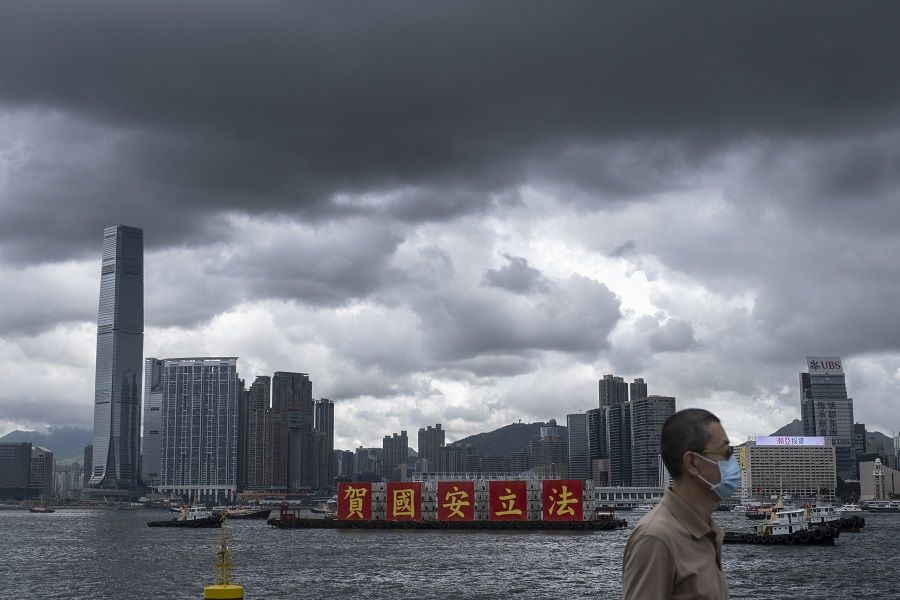 A man wearing a protective mask walks by the waterfront as a barge sails past with a message celebrating the passage of the new national security law in Hong Kong, China, 1 July 2020. (Roy Liu/Bloomberg)