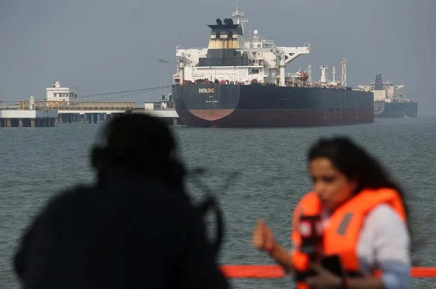 Journalists report in front of the Liberia-flagged tanker Shenlong Suezmax, loaded with Saudi Arabian crude, after it arrived at a port after transiting the Strait of Hormuz amid supply disruptions linked to the US-Israeli conflict with Iran, in Mumbai, India, on 12 March 2026. (Reuters)
