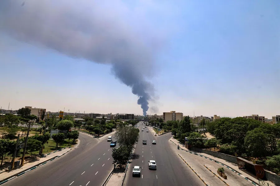 Commuters drive along a road as a plume of heavy smoke and fire rise from an oil refinery in southern Tehran, after it was hit in an overnight Israeli strike, on 15 June 2025.