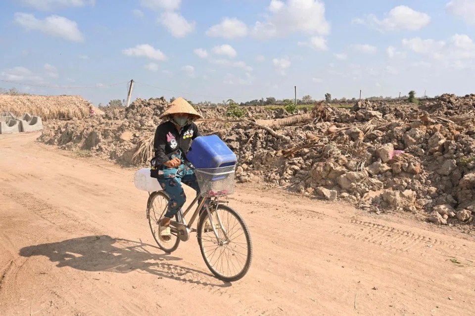 A woman rides a bicycle carrying plastic cans for fresh water, in Vietnam's southern Ben Tre province on 19 March 2024. (Nhac Nguyen/AFP)