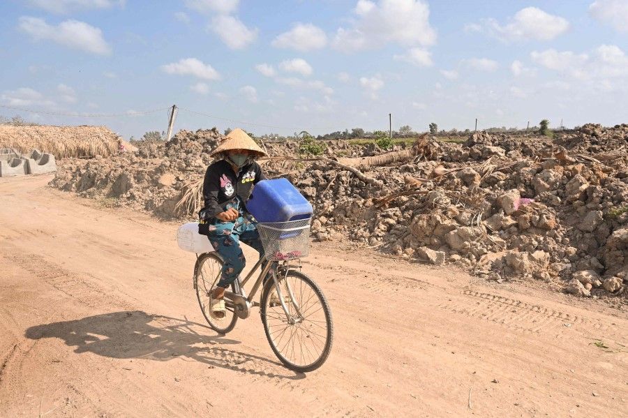 A woman rides a bicycle carrying plastic cans for fresh water, in Vietnam's southern Ben Tre province on 19 March 2024. (Nhac Nguyen/AFP)