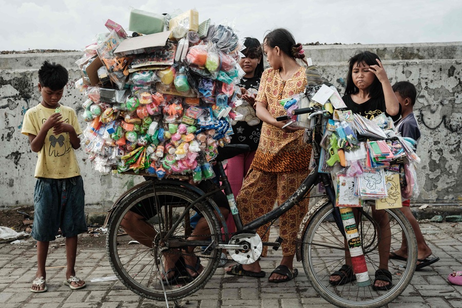 Children buy toys piled high on a bicycle next to a seawall in Cilincing, north Jakarta, on 20 September 2025. (Yasuyoshi Chibi/AFP)