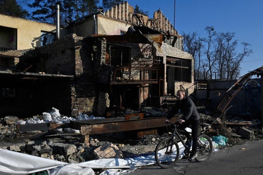 A cyclist rides on a bicycle past a house destroyed by shelling in Hostomel near Kyiv, on 19 March 2023, amid the Russian invasion of Ukraine. (Sergei Chuzavkov/AFP)