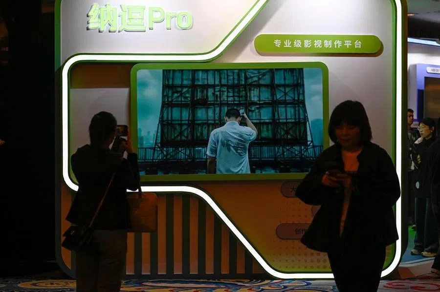 People walk past a TV screen showing a video of Nadou pro, iQiyi’s AI product for professional film and television production, during the iQiyi World Conference in Beijing on 20 April 2026. (Wang Zhao/AFP)