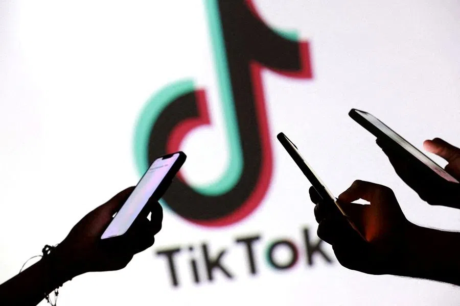 Teenagers pose for a photo while holding smartphones in front of a TikTok logo in this illustration taken 11 September 2025.