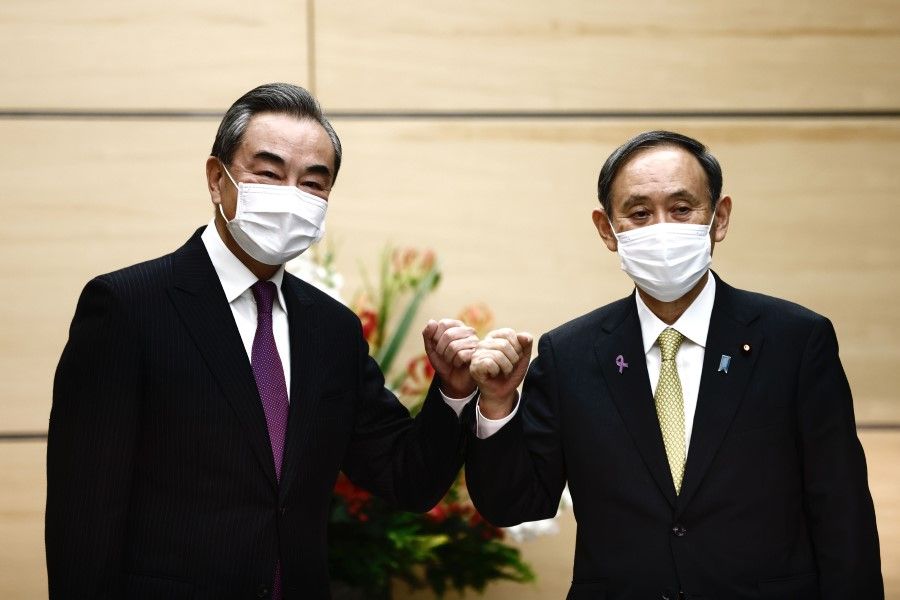 Japan's Prime Minister Yoshihide Suga (right) bumps elbows with China's State Councilor and Foreign Minister Wang Yi at the start of their meeting in Tokyo on 25 November 2020. (Behrouz Mehri/AFP)