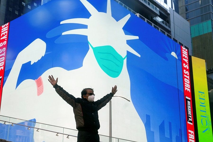 A man poses for a photo on the Red Steps in Times Square as an image of the Statue of Liberty wearing a mask is projected on a billboard amid the Covid-19 pandemic in the Manhattan borough of New York City, New York, US, 20 April 2021. (Carlo Allegri/Reuters)