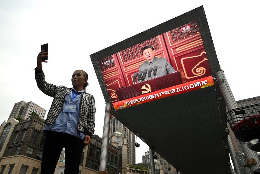 A woman takes a selfie as Chinese President Xi Jinping's speech is broadcast on a large screen in Beijing, China during the 100th anniversary of the founding of the Communist Party of China on 1 July 2021. (Noel Celis/AFP)