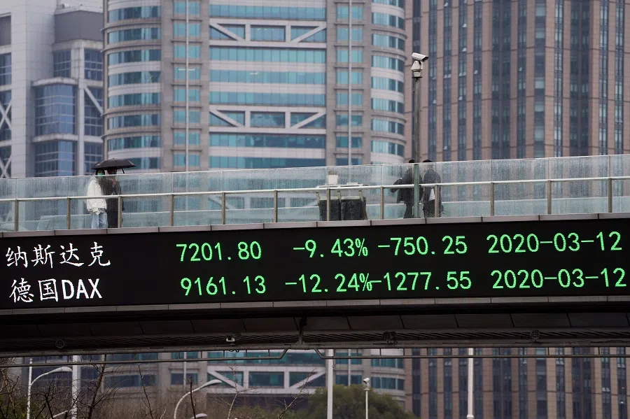 People wearing face masks walk on a pedestrian overpass with an electronic board showing stock indexes, following the Covid-19 outbreak, at Lujiazui financial district in Shanghai, China, on 13 March 2020. (Aly Song/Reuters)
