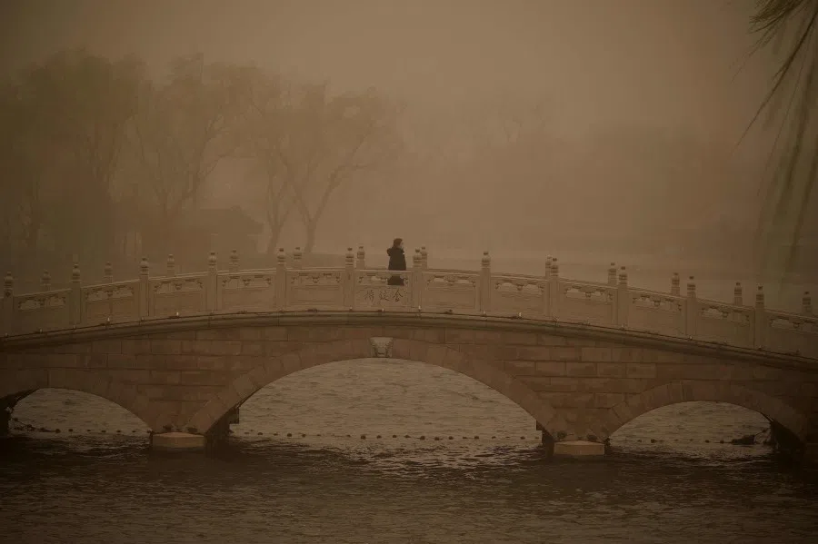 A woman crosses a bridge at Houhai lake during a sandstorm in Beijing on 15 March 2021. (Noel Celis/AFP)