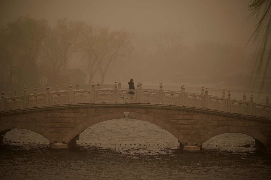 A woman crosses a bridge at Houhai lake during a sandstorm in Beijing on 15 March 2021. (Noel Celis/AFP)