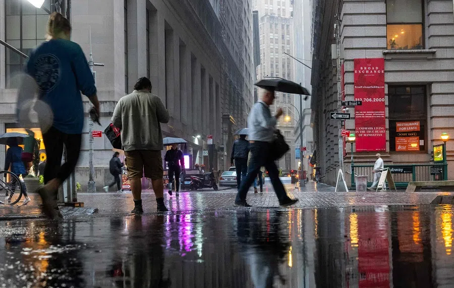 People walk through the morning rain by the New York Stock Exchange (NYSE) on 20 October 2023 in New York City, US. (Spencer Platt/Getty Images/AFP)
