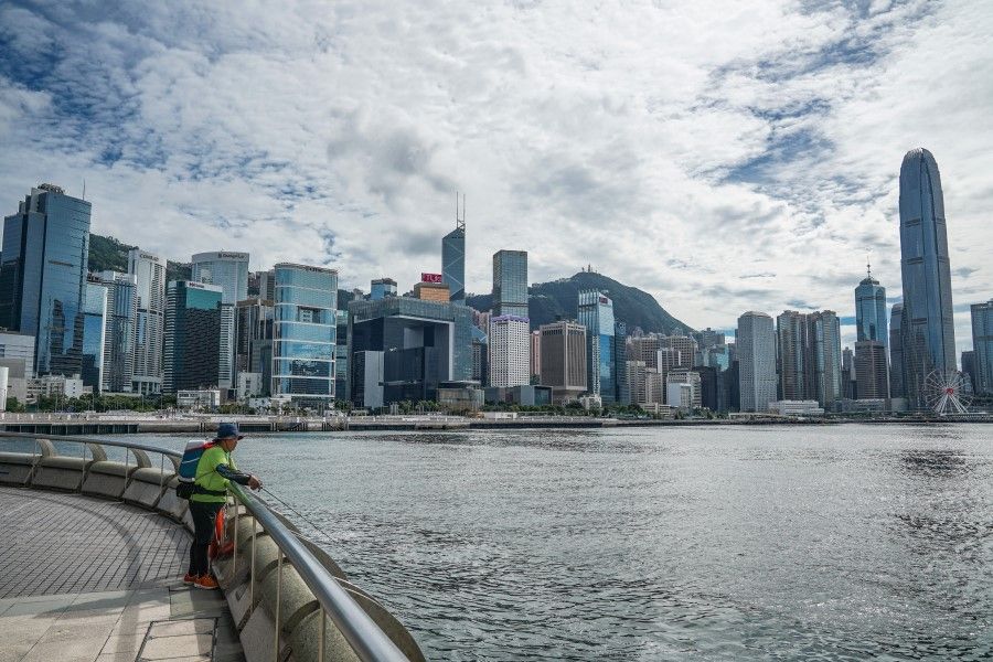 An angler fishes as buildings stand across the Victoria Harbor in Hong Kong, China, 15 July 2020. (Lam Yik/Bloomberg)