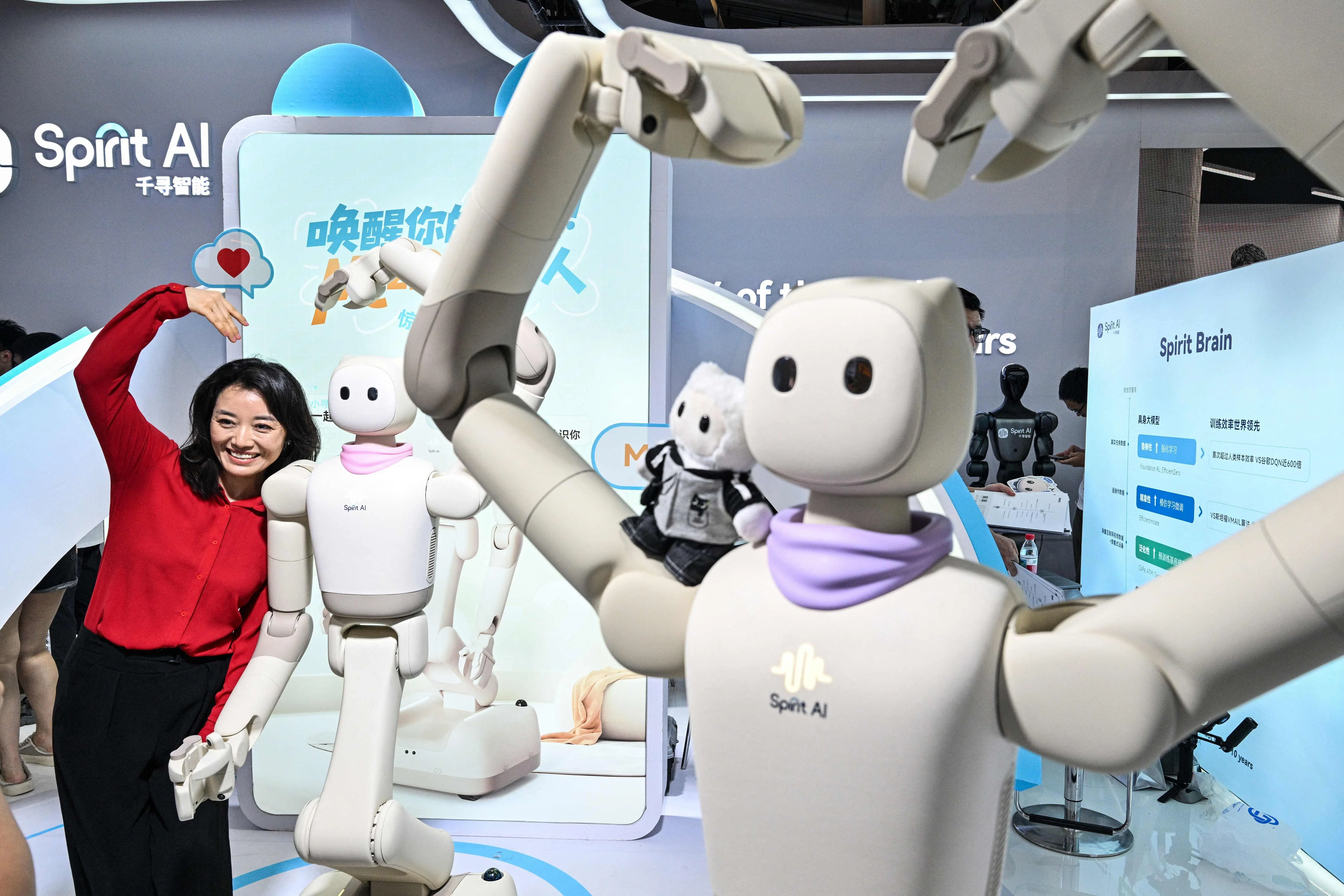 A woman poses next to humanoid robots by Spirit AI during the World Artificial Intelligence Conference (WAIC) in Shanghai on 18 July 2026.