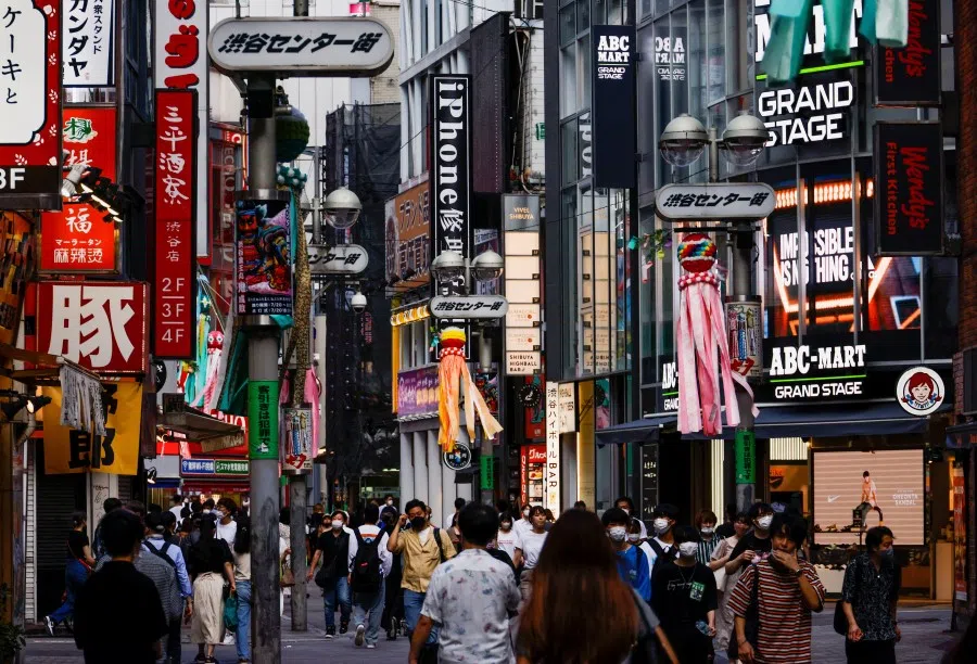 Passersby wearing protective face masks walk on the street at Shibuya shopping and amusement district, amid the Covid-19 pandemic, in Tokyo, Japan, 28 July 2022. (Issei Kato/Reuters)