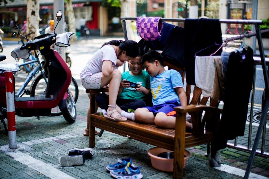 Children look at a phone on a street in Shanghai, China, 28 August 2021. (Aly Song/Reuters)