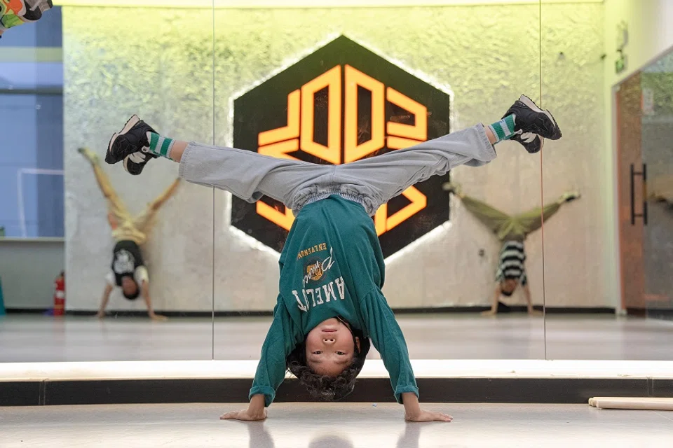 Zhuangzhuang is doing physical training in a breaking class. Handstands can help him train upper body strength, which is essential in breaking.