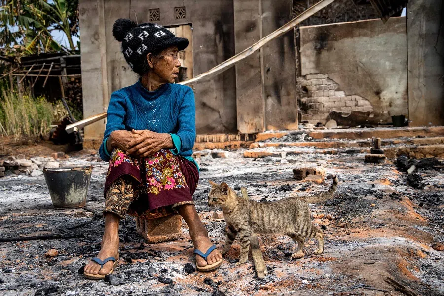 This photo taken on 4 February 2024 shows a woman sitting next to a cat in front of her house damaged following fighting between Myanmar's military and the Kachin Independence Army (KIA) in Nam Hpat Kar, Kutkai township in Myanmar's northern Shan State. In late October, an alliance of ethnic minority fighters launched a surprise offensive in northern Shan state, capturing territory and taking control of lucrative trade routes to China. (AFP)