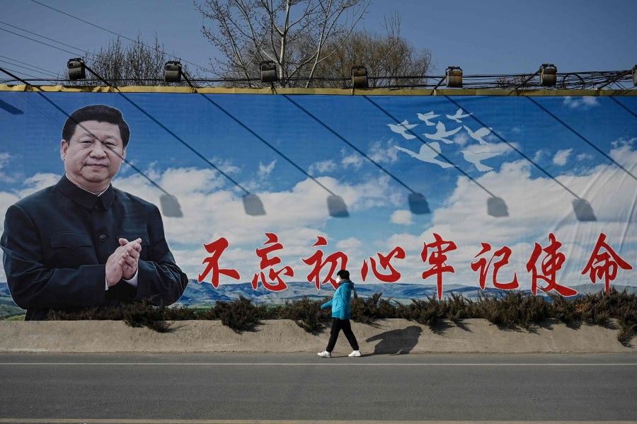 A woman walks past a billboard showing Chinese President Xi Jinping with a slogan which reads "Remain true to our original aspiration and keep our mission firmly in mind" in Beijing on 28 February 2023. (Jade Gao/AFP)