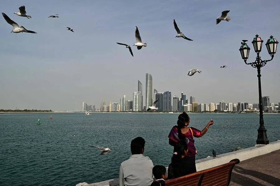 A woman feeds seagulls along a promenade overlooking the Abu Dhabi skyline on 23 January 2026. (Giuseppe Cacace/AFP)