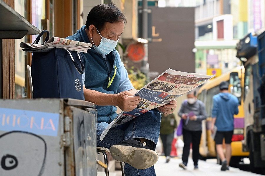This photo taken on 6 January 2022 shows a man reading a newspaper on a sidewalk in Hong Kong. (Peter Parks/AFP)