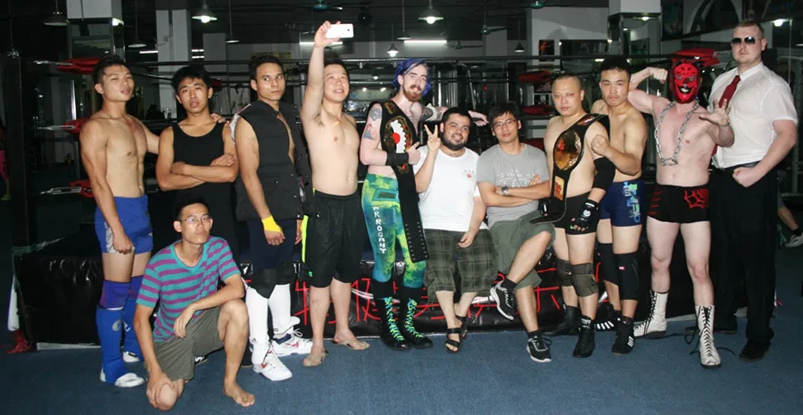 A group of wrestlers pose for a ringside picture with Adrian Gomez (centre) and The Slam (fourth from right, with belt).