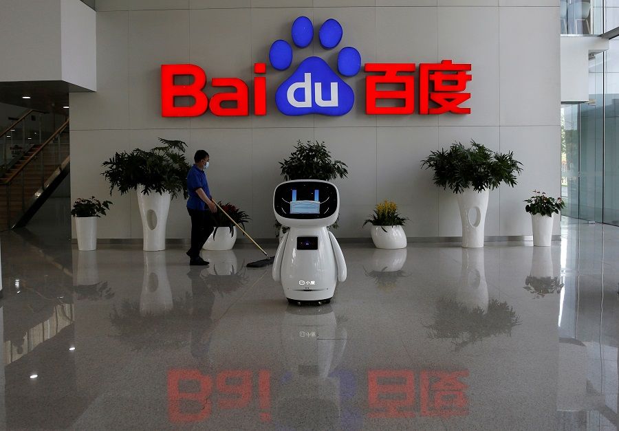 A worker wearing a face mask cleans the floor, near a Baidu AI robot which shows a face mask on its screen, at Baidu's headquarters in Beijing, China, 18 May 2020. (Tingshu Wang/File Photo/Reuters)