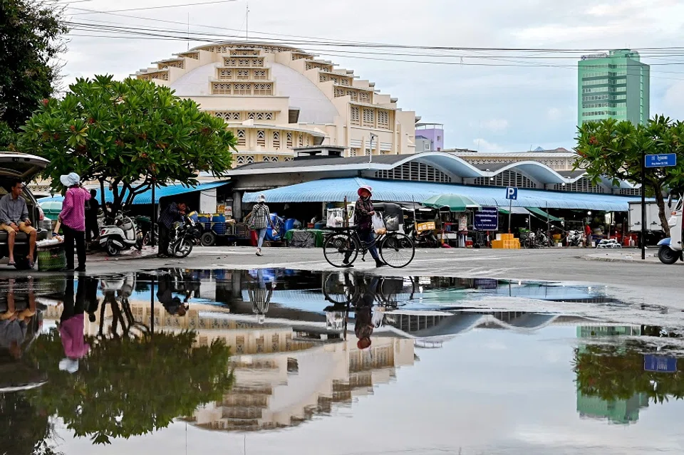 A vendor (centre) pushes her bicycle loaded with food for sale along a street near the Central Market in Phnom Penh, Cambodia, on 27 June 2024. (Tang Chhin Sothy/AFP)