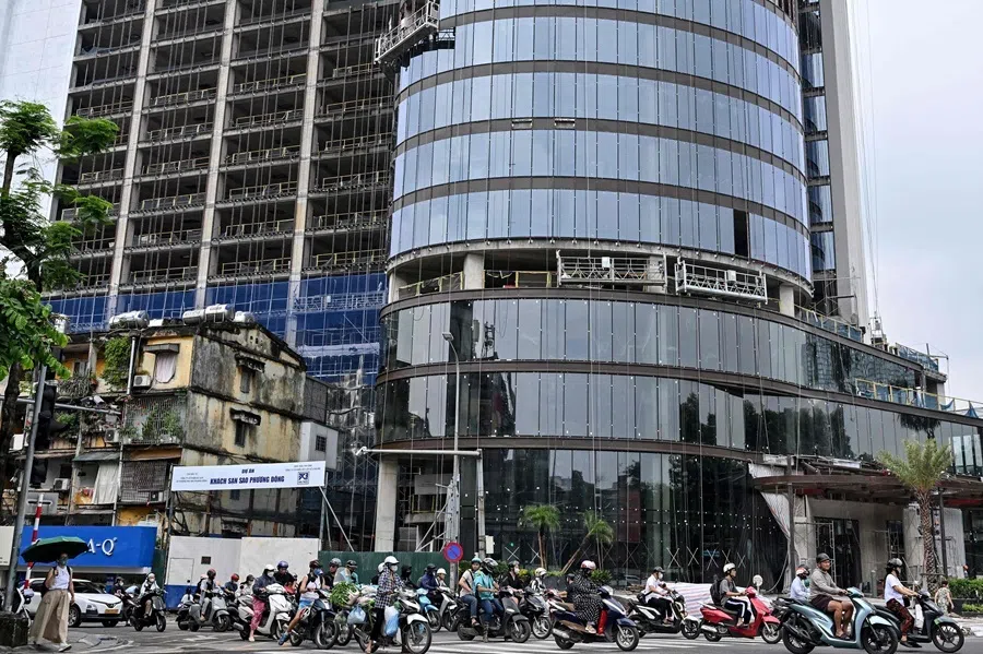 People ride their motorbike past a hotel construction site in Hanoi on 10 July 2026.