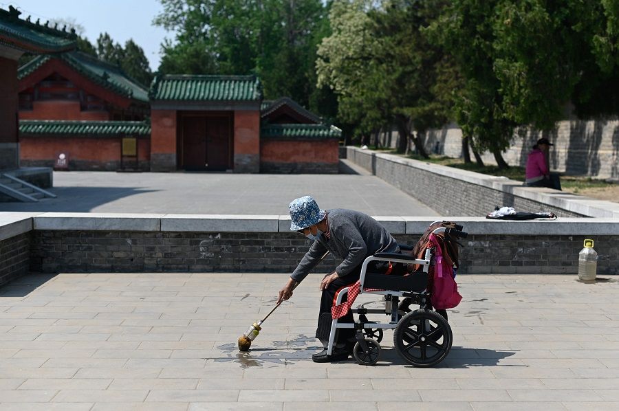 An elderly woman wearing a face mask practises water calligraphy on a pavement in Beijing on 27 April 2020. (Wang Zhao/AFP)