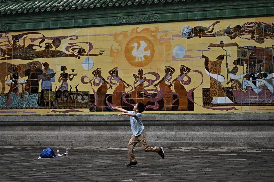 A boy plays badminton next to a mural in Ritan Park in Beijing on 23 August 2025. (Pedro Pardo/AFP)