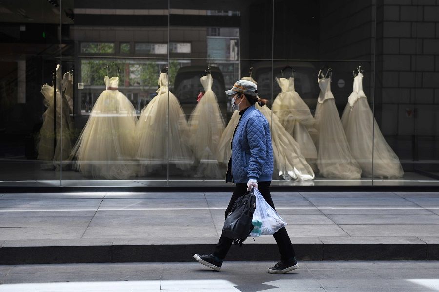 A woman wearing a face mask amid the Covid-19 pandemic walks past wedding dresses displayed in a Vera Wang bridal store in Beijing on 22 April 2020. (Greg Baker/AFP)