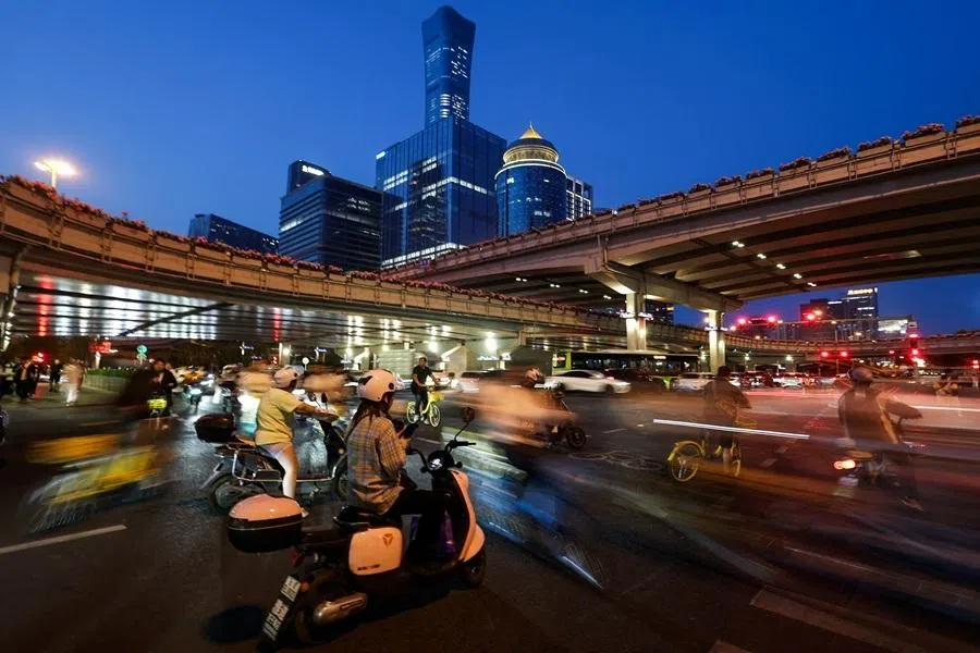 People ride scooters and bicycles at a junction, with skyscrapers of Beijing’s central business district seen in the background, in Beijing, China, 11 May 2026.