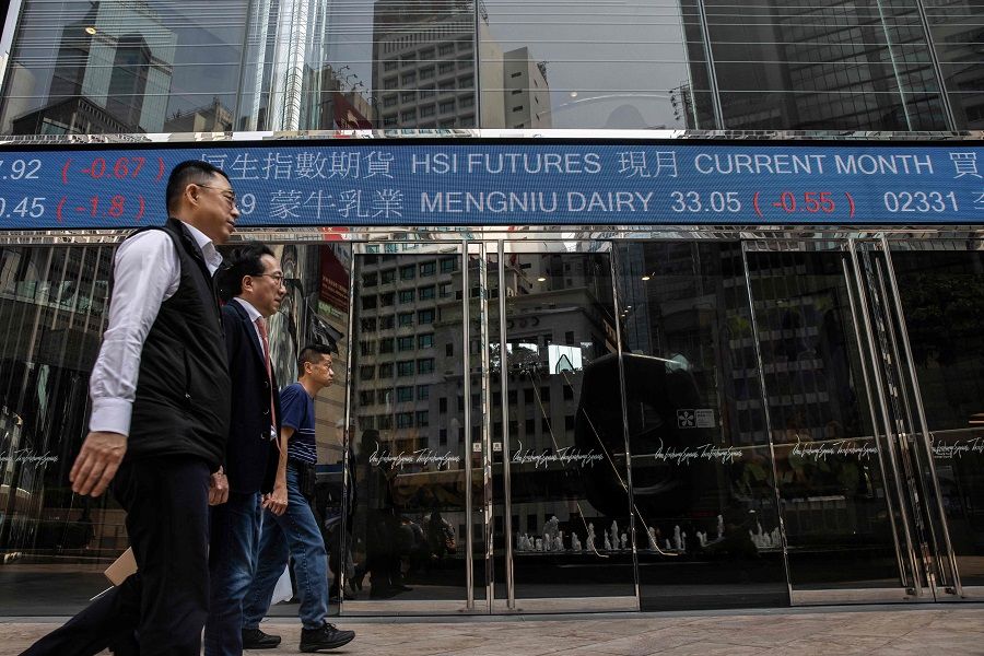 People walk past an electronic sign displaying stocks at Exchange Square in Hong Kong, China, on 16 March 2023. (Isaac Lawrence/AFP)