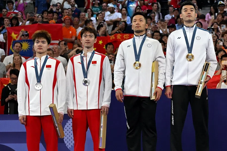 Taiwan’s gold medallists (right) Lee Yang and Wang Chi-lin and China’s silver medallists Liang Weikeng and Wang Chang stand up for the anthem of Chinese Taipei on the podium at the men’s doubles badminton medal ceremony during the Paris 2024 Olympic Games at Porte de la Chapelle Arena in Paris on 4 August 2024. 