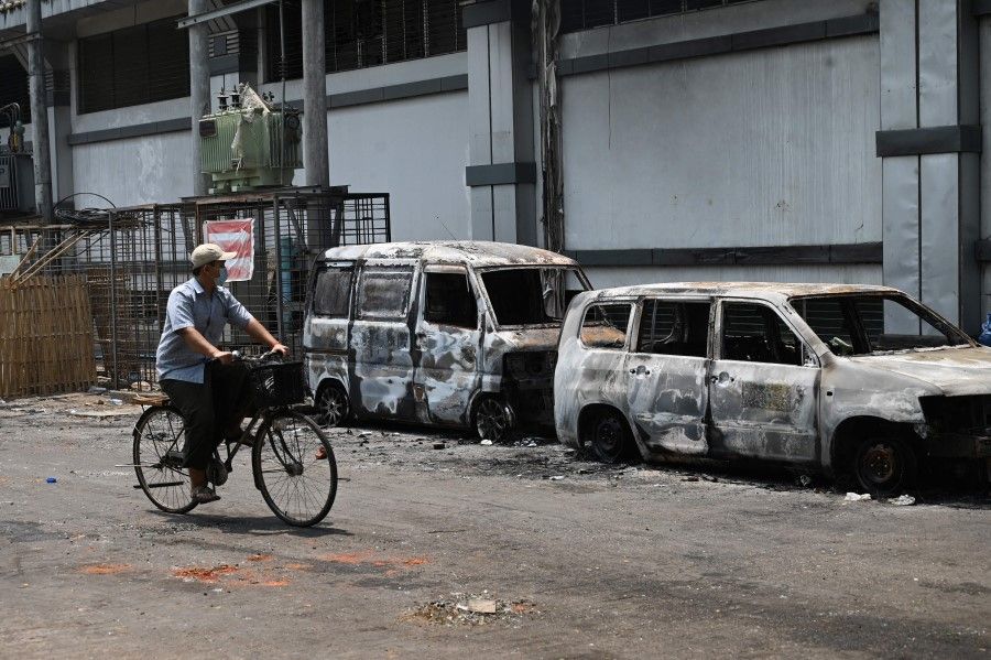 A man cycles past burnt vehicles in the aftermath of a fire amid a crackdown by security forces on demonstrations against the military coup, in Yangon on 15 March 2021. (STR/AFP)