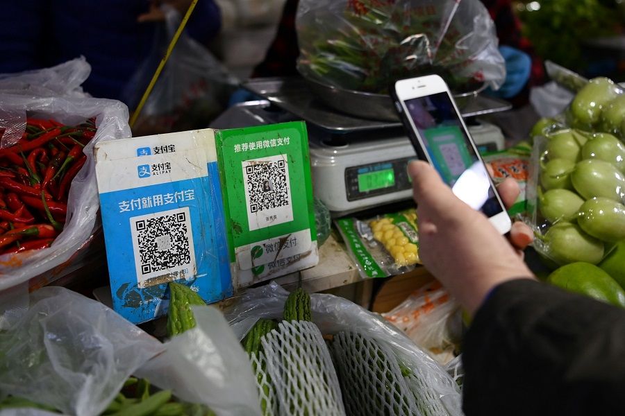 A customer makes a payment using a Wechat QR payment code (centre) via her smartphone, next to an Alipay QR code (left), at a vegetable market in Beijing on 3 November 2020. (Greg Baker/AFP)