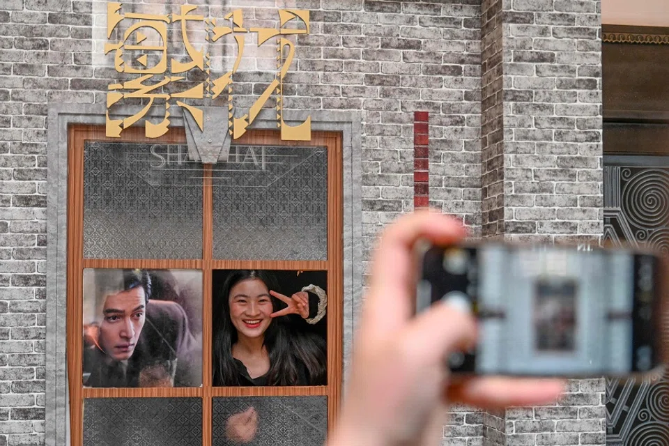 The photo taken on 7 January 2024 shows a woman posing for photos next to a poster of Chinese television series Blossoms Shanghai. (AFP)